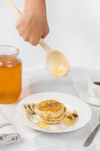 Pilha de panquecas empilhadas com rodelas de banana e um fio de mel ao lado.